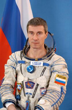 Krikalev posing in a space suit in front of the Russian flag