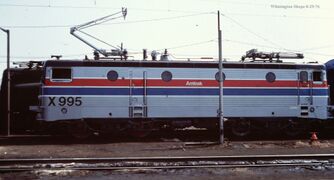 A gray electric locomotive with a black roof and red and blue side stripes