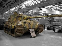 A large, turreted tank with dull yellow, green and brown wavy camouflage, on display inside Bovington museum. The tracks are wide, and the frontal armour is sloped. The long gun overhangs the bow by several meters.