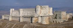 Photograph of 12th-century Hospitaller castle of Krak des Chevaliers in Syria showing concentric rings of defence, curtain walls and location sitting on a promontory.
