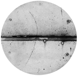 track of subatomic particle moving upward through cloud chamber and bending left (an electron would have turned right)