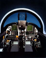 Mock-up of jet fighter's cockpit, featuring a head-up display behind windshield and displays and dials in front of the pilot.