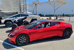 A stainless steel clad ATV between a Tesla Cybertruck and a second generation Tesla Roadster in a parking lot during a Tesla event in 2020.