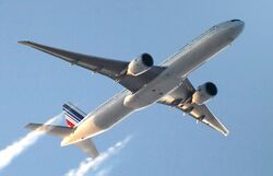 Twin-engine aircraft in flight, quarter belly view, with contrails