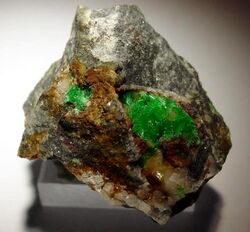 bright green crystals in two clusters on a white and grey rock