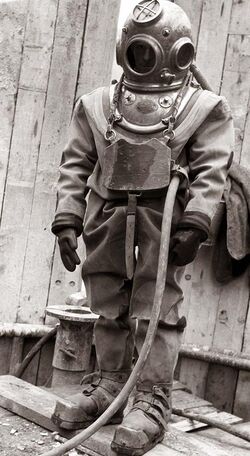 Standing figure of a diver clad in copper helmet, heavy canvas diving suit, with gloves, chest weight and weighted boots