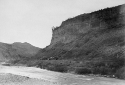 Black and white photo of a river with rocky cliffs in the background.