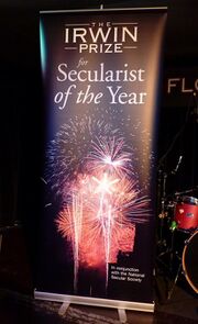 A roll-up banner reading "The Irwin Prize for Secularist of the Year" in a dark venue