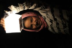 14 year old Syrian refugee girl at night dressed with a head scarf is illuminated by holding up a Solar lantern called SolarPuff in the Idomeni refugee camp in Greece 2015