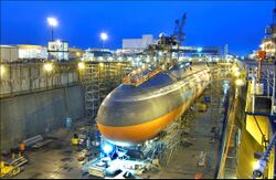 Black submarine with orange paint from cheatline down in drydock at nightfall