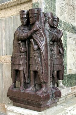 A sculpture of four men, each holding a sword, forming two pairs embracing each other.