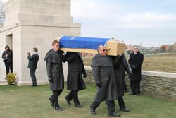 four men dressed entirely in black are carrying a wood casket draped in a flag.
