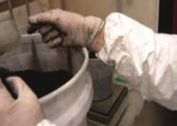 A closeup of a person's arm requing into a bucket filled with a black material