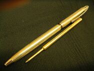 Full length view of gold colored pen body showing nib end nearest with refill laid into alignment underneath