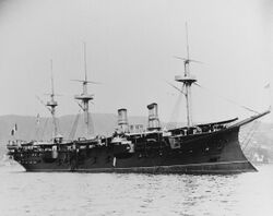 A large black ship with two smoke stacks and three masts sits offshore; mountains are visible in the background.