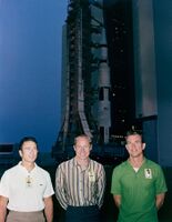 Three men stand in front of a rocket
