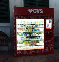 A large red vending machine with common pharmacy products visible through the glass