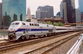 A light gray diesel locomotive with a blue stripe and two thinner red stripes on the side. The stripes narrow and angle downwards on the front.