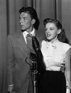 Photograph of a man with his arm wrapped around a woman, both in front of a microphone