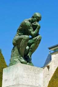 Statue of the Thinker, a nude seated man, against a blue sky