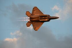USAF F-22 Raptor flying in knife edge during a high-speed low-altitude pass over Airventure in full afterburner with Mach diamonds at sunset