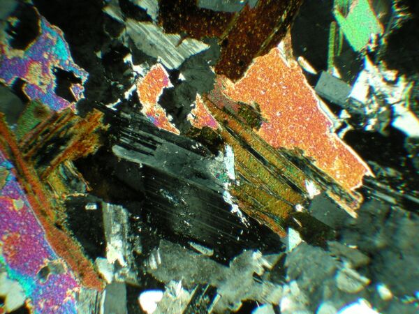 Granite sample under cross polarized light containing plagioclase, quartz, and mica. The mica in orange here exhibits the bird's eye extinction pattern.
