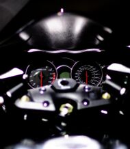 The speedometer and tachometer of a motorcycle with the triple clamp in the foreground. The tachometer goes to 11,000 and the speedometer to 180 mph