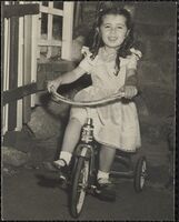 Girl with ringlets and a white dress riding a delta tricycle.
