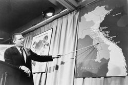 Robert McNamera pointing to a map of Vietnam at a press conference, 1965.JPG