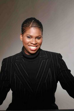 An African-American woman known as Vanessa Braxton poses for a photo wearing a black turtleneck and a black blazer with small grey stripes going down vertically.