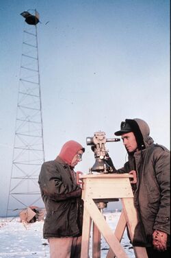 Picture of a man taking measurements with a theodolite in a frozen environment.