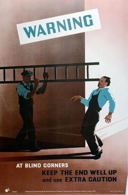 A man carrying a ladder around a corner accidentally strikes the eye of a man approaching around the corner from the right side of the image, as shown by little dashes. They wear overalls suggesting a workplace uniform. Text warns to use caution at corners.