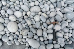 A rock hammer rests atop a variety of well-rounded gray cobbles.