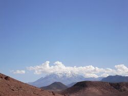 Brown, barren hills with two snow-covered mountains rising above them