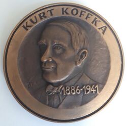 A bronze medallion with an outer ring containing the text "KURT KOFFKA" at the top, containing a central embossed image of a three-quarter face and upper chest of Kurt Koffka looking to the right. Superimposed on the chest and to the left of the midline is the text "1886-1941"