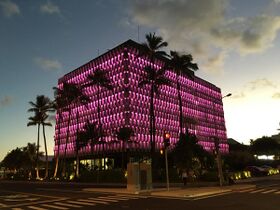 The IBM building, a roughly cube-shaped building with a honeycomb patterned grille around it. In this image it is lit up pink.