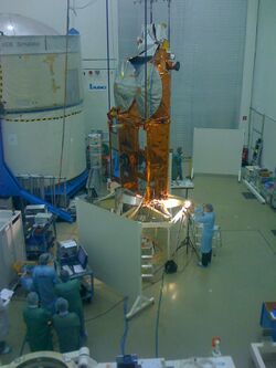 A group of people looking at a gold spacecraft on a stand in the middle of a room