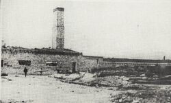 A black-and-white photograph of a low building with a tall chimney. The structure served as a crematorium.