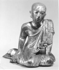 Wooden sculpture of monk sitting in a mermaid pose, reclining