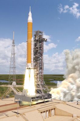 A large orange and white rocket launching off pad 39B at Kennedy Space Center beside a tall steel support tower