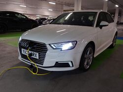 A white Audi A3 e-tron is plugged into a public charge point.