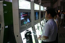 A man and other gamers play Project Sylpheed, which is running on a line of four upright cabinets that each holds an Xbox 360 game console and a LCD display.
