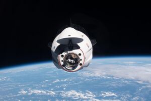 A Crew Dragon spacecraft can be seen with the Earth in the background