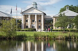 A large academic building with students and a pond in the foreground.