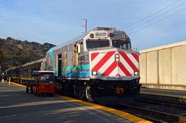 A locomotive painted gray with turquoise and light blue stripes and a curve towards the top rear of the locomotive, with red chevron stripes on the front.