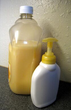 A refillable liquid pump soap dispenser. Next to it is a larger bottle containing the same type of soap.