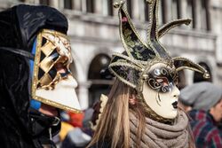 Two people obscuring their faces with festive masks during a Carnival celebration.