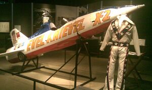 Rocket with front end tilted upwards and a flight suit in front of it