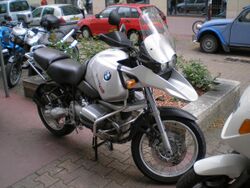 Silver BMW R1150GS parked on a city street with other cars and bikes in the background