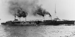 A large, black ship steams at high speed, thick black smoke billowing from its four widely spaced funnels.